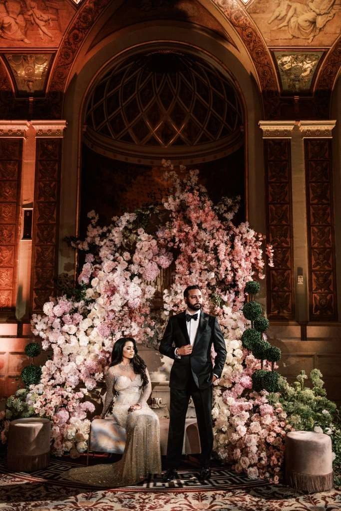 A couple dressed for an evening celebration before a floral installation