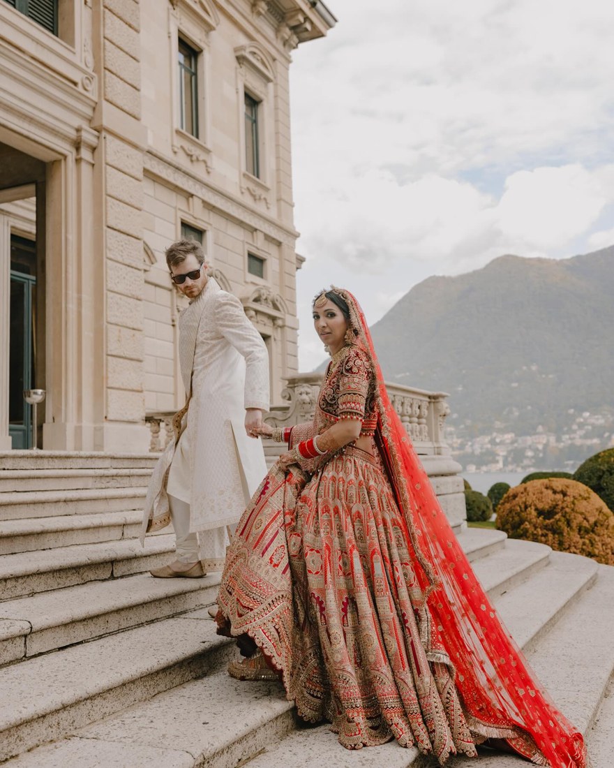 A couple in traditional Indian wedding attire beside an Italian lakeside villa