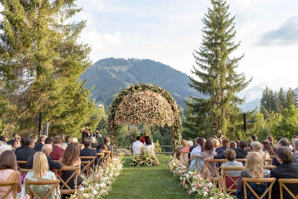 Wedding guests gathered for a mountain ceremony beneath a floral arch